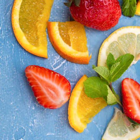 An assortment of different fruits and berries. Strawberries, slices of orange, lemon and mint...
