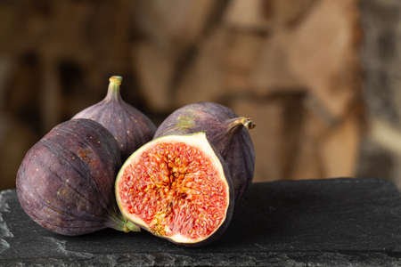 Three whole and one cut ripe organic figs on dark rough stone and blurred wooden backgroundの写真素材