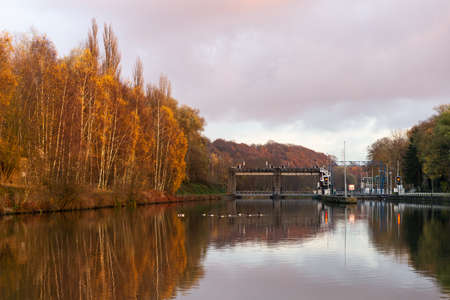 Ship lock on the river with yellow autumn trees along the shore and wild geese floating on the waterの写真素材