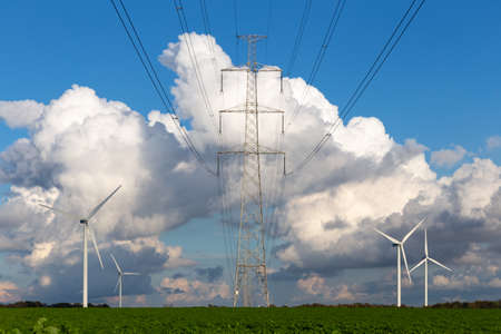 high-voltage power line tower and wind generators in a green field and with a beautiful cloudy blue skyの写真素材