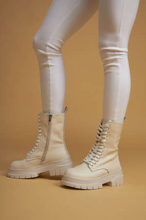 Fashionable woman with beige boots, leather shoes, studio shot. Casual lifestyle concept photo on a yellow background.の写真素材