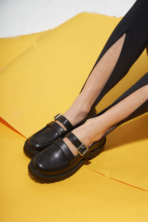 Woman chooses shoes collection autumn spring 2022. Long slim beautiful female feet. Sexy fashion model woman legs with black shoes on sunny background. Fashion model girl legs portrait on yellow background. Beauty stylish woman wear woman posing in fashion clothes in studio. Summer fashion, trendy bag and shoes, casual style.の写真素材
