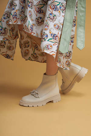 Fashionable woman with beige boots, leather shoes, studio shot. Casual lifestyle concept photo on a yellow pastel background.の写真素材