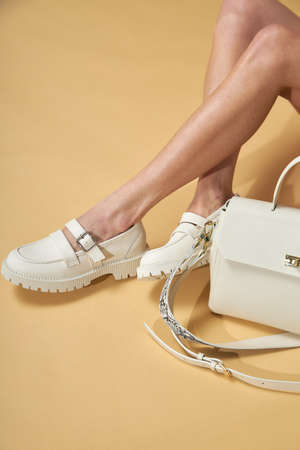 Fashionable woman with beige boots, leather shoes, studio shot. Casual lifestyle concept photo on a yellow pastel background. Fashionable handbag and shoes setの写真素材