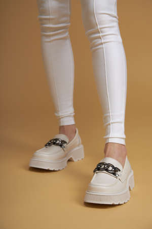 Perfect female legs.  Beautiful female legs in summer shoes in white designer pants on a yellow pastel  background.の写真素材