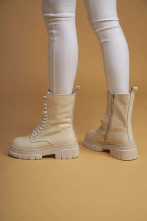 Fashionable woman with beige boots, leather shoes, studio shot. Casual lifestyle concept photo on a yellow pastel background. Fashion shoes made of eco-leather spring-summer 2022.の写真素材