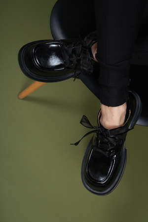 Female legs in black boots on green background. Casual lifestyle concept photo. Fashion shoes made of eco-leather spring-summer 2022.の写真素材
