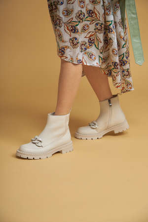 Fashionable woman with beige boots, leather shoes, studio shot. Casual lifestyle concept photo on a yellow pastel background. Fashion shoes made of eco-leather spring-summer 2022.の写真素材