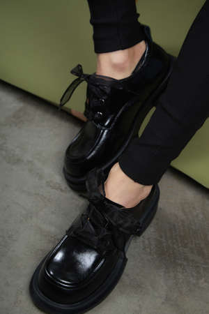 Female legs in black boots on green background. Casual lifestyle concept photo. Fashion shoes made of eco-leather spring-summer 2022.の写真素材