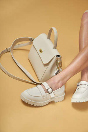 Fashionable woman with beige boots, leather shoes, studio shot. Casual lifestyle concept photo on a yellow pastel background. Fashionable handbag and shoes setの写真素材