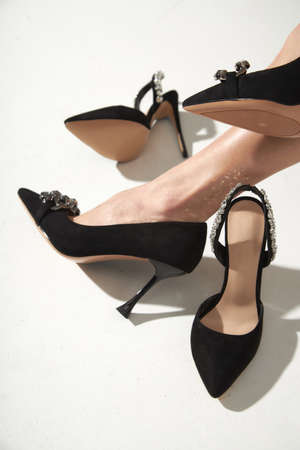 Woman taking off black high heels shoes. Long slim beautiful female feet in footwear, isolated on a white background.の写真素材