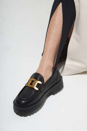 Beauty stylish woman posing in fashion clothes in studio. Summer fashion, trendy shoes, casual style. Woman chooses shoes collection autumn spring 2022. Long slim beautiful female feet. Sexy fashion model woman legs with black shoes on white background.の写真素材