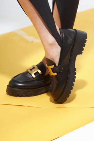 Beauty stylish woman posing in fashion clothes in studio. Summer fashion, trendy shoes, casual style. Woman chooses shoes collection autumn spring 2022. Long slim beautiful female feet. Sexy fashion model woman legs with black shoes on sunny background.の写真素材