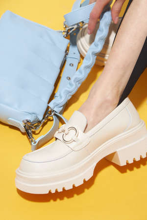 Woman chooses shoes collection autumn spring 2022. Long slim beautiful female feet. Sexy fashion model woman legs with black shoes on sunny background. Fashion model girl legs portrait on yellow background. Beauty stylish woman wear woman posing in fashion clothes in studio. Summer fashion, trendy bag and shoes, casual style. Fashionable handbag and shoes setの写真素材