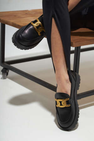 Beauty stylish woman posing in fashion clothes in studio. Summer fashion, trendy shoes, casual style. Woman chooses shoes collection autumn spring 2022. Long slim beautiful female feet. Sexy fashion model woman legs with black shoes on white background.の写真素材