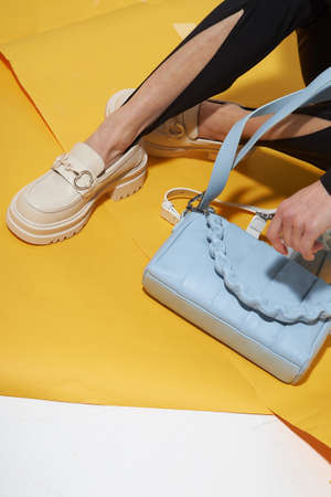 Woman chooses shoes collection autumn spring 2022. Long slim beautiful female feet. Sexy fashion model woman legs with black shoes on sunny background. Fashion model girl legs portrait on yellow background. Beauty stylish woman wear woman posing in fashion clothes in studio. Summer fashion, trendy bag and shoes, casual style. Fashionable handbag and shoes setの写真素材