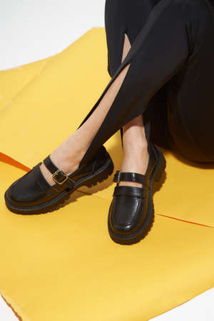 Woman chooses shoes collection autumn spring 2022. Long slim beautiful female feet. Sexy fashion model woman legs with black shoes on sunny background. Fashion model girl legs portrait on yellow background. Beauty stylish woman wear woman posing in fashion clothes in studio. Summer fashion, trendy bag and shoes, casual style.の写真素材