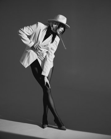 Fashion shoot. Portrait of a beautiful girl in a white hat with a scarf and a jacket. Vogue trend. Young woman is posing in a studioの写真素材