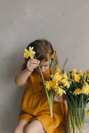 little girl in a yellow dress with a beautiful bouquet of narcissus flowerの写真素材