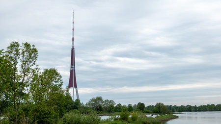 Riga Radio and TV Tower near Daugava river with green trees.