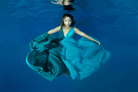 Young beautiful woman with long hair in a bright green-blue dress under water, underwater fashion in the pool, Odessa, Ukraineの写真素材