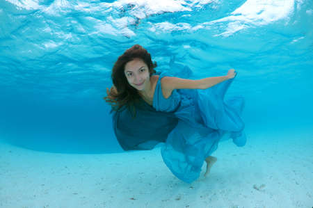 Young beautiful woman with long hair in a bright green-blue dress under water, underwater fashion in the Indian Ocean, Maldivesの写真素材