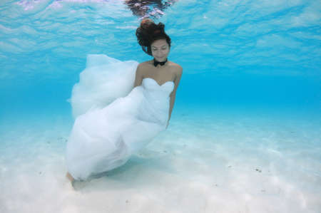 Young beautiful woman with long hair in a long white wedding dress under water, underwater wedding in the Indian ocean, Maldivesの写真素材