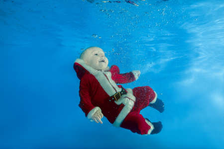 A little boy in Santa's cost swims underwater in the poolの写真素材