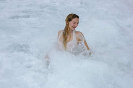 Young woman in a white shirt is bathed in the ocean