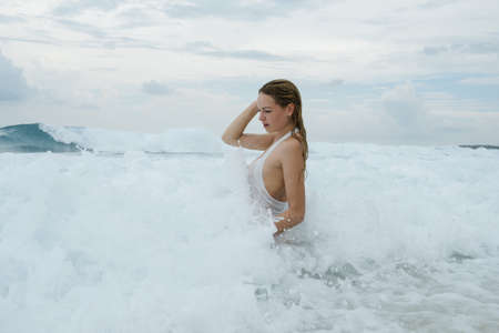 Young woman in a white shirt is bathed in the oceanの写真素材