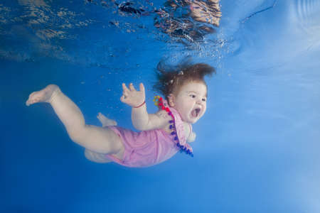 Little girl with an open mouth swimming underwater in the poolの写真素材