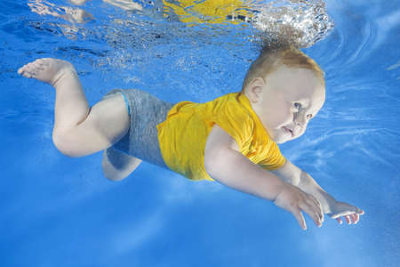 little boy in a yellow shirt learns to swim underwater in the poolの写真素材
