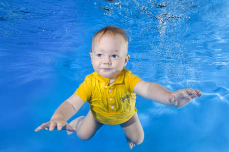 little boy in a yellow shirt learns to swim underwater in the poolの写真素材