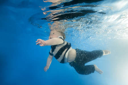  little boy in a suit swims underwater in the pool