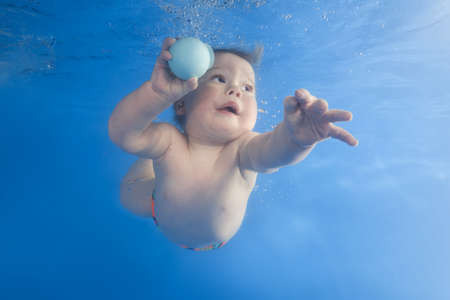 little boy playing with ball underwater in the poolの写真素材