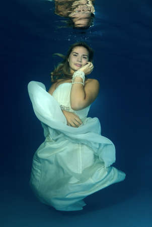 Young beautiful woman in white wedding dress underwaterの写真素材