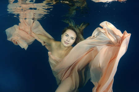 Young beautiful woman in a long dress underwaterの写真素材