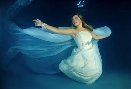 Young beautiful woman in white wedding dress underwaterの写真素材