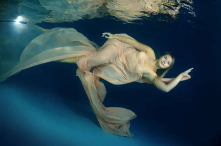 Young beautiful woman in a long dress underwaterの写真素材
