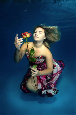 Young beautiful woman in a bright dress with a rose in hands underwaterの写真素材