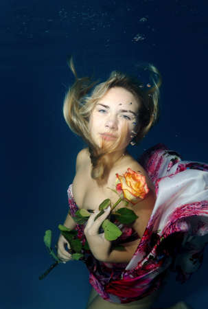 Young beautiful woman in a bright dress with a rose in hands underwaterの写真素材
