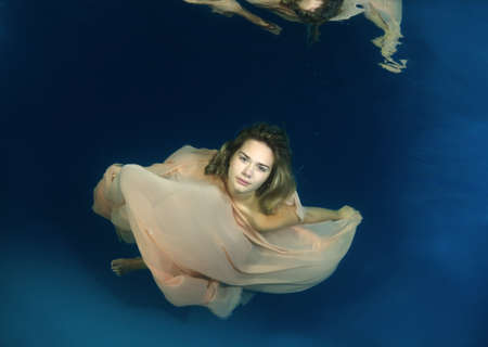 Young beautiful woman in a long dress underwaterの写真素材
