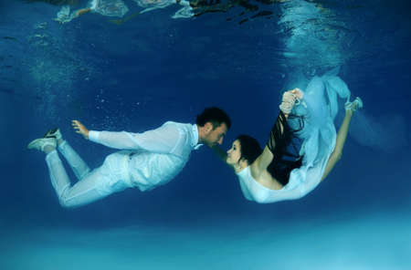Bride and groom in a white wedding dress swim to each other underwater in the pool. Underwater weddingの写真素材