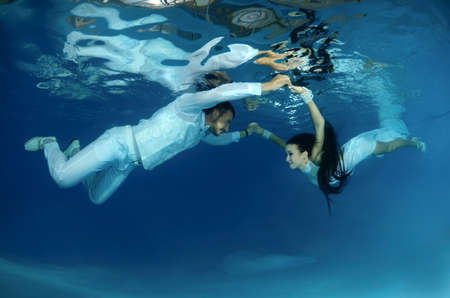 Bride and groom in a white wedding dress swim to each other underwater in the pool. Underwater weddingの写真素材