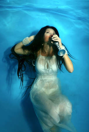 Bride is drinking red wine under the water in the pool . Underwater wedding の写真素材