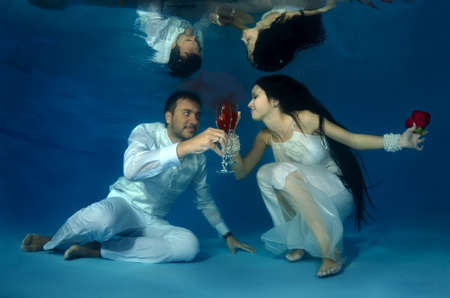Bride and groom drink red wine underwater in the pool. Underwater wedding の写真素材