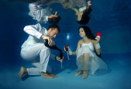 Bride and groom drink red wine underwater in the pool. Underwater wedding の写真素材