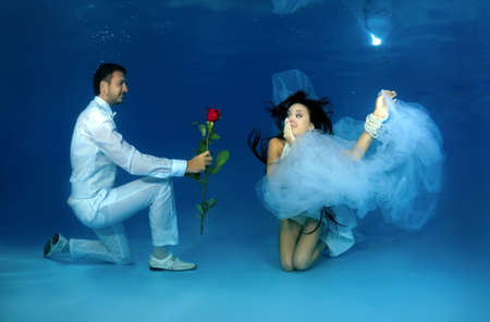 Groom kneeling gives flowers to the bride underwater in the pool. Underwater wedding の写真素材
