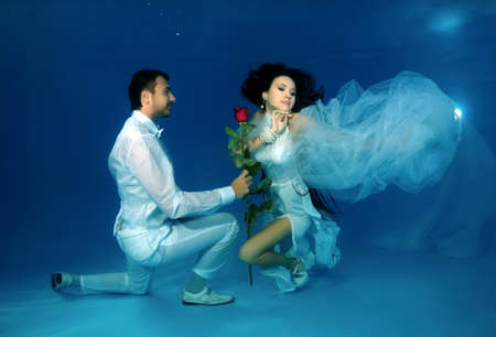 Groom kneeling gives flowers to the bride underwater in the pool. Underwater wedding の写真素材