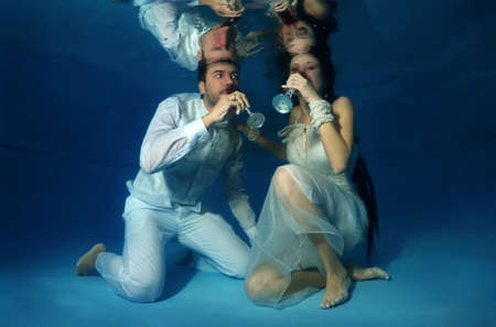 Bride and groom drink red wine underwater in the pool. Underwater wedding の写真素材
